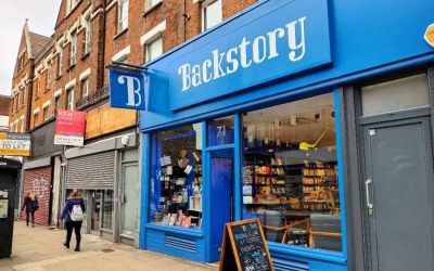 The shop front of Backstory is bright blue. The window displays a collection of fiction by women and a sign outside advertises events.