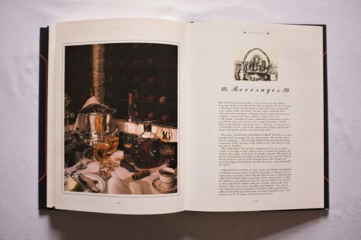 The first two pages of Chapter 14 of The Shorter Mrs. Beeton, on Beverages, are dominated by a full-page colour photograph from a butler’s pantry incorporating a wine rack, decanters and rummers, a silver-plated champagne bucket, corkscrew, cup of coffee and dessert plate with an apple and dessert knife. 