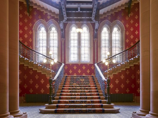 The grand staircase at the St Pancras hotel is profusely decorated and lit with slender Gothic windows.