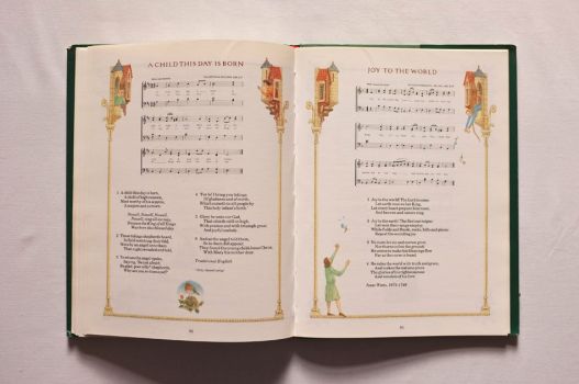 An illuminated double-page spread from A Book of Christmas Carols carries the words and music of A Child This Day Is Born and Joy to The World.  