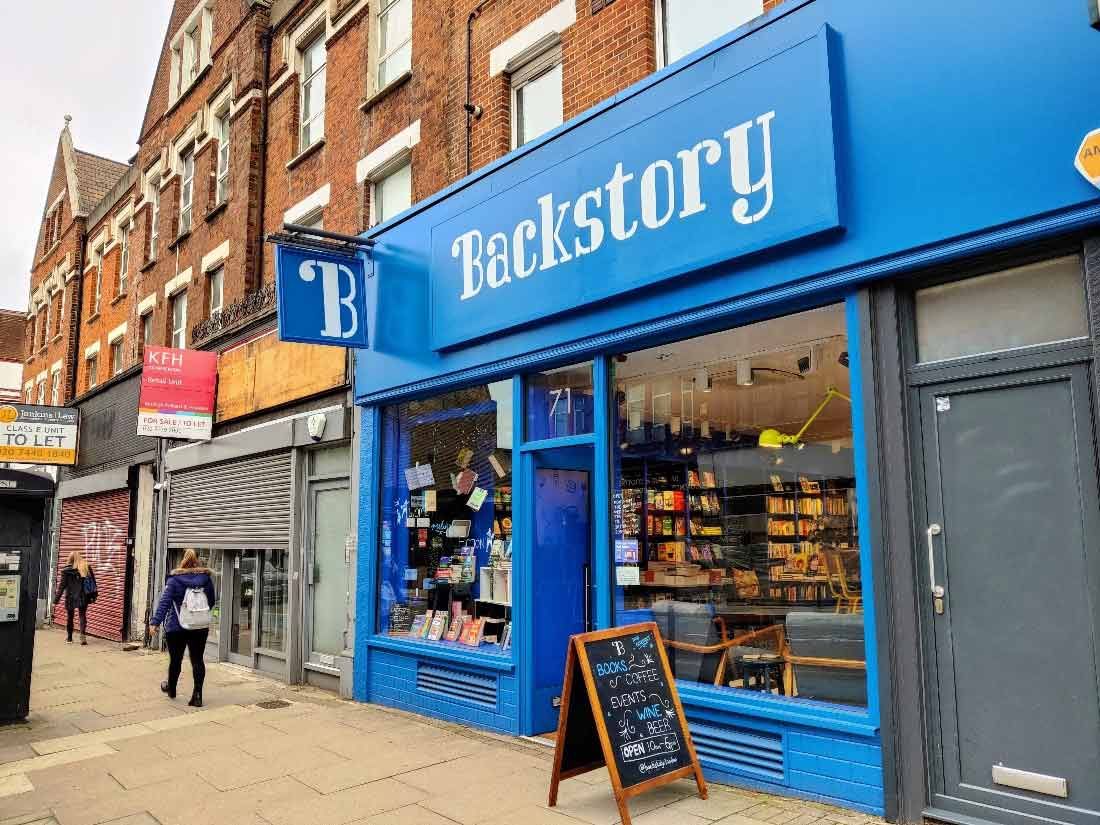 The shop front of Backstory is bright blue. The window displays a collection of fiction by women and a sign outside advertises events.