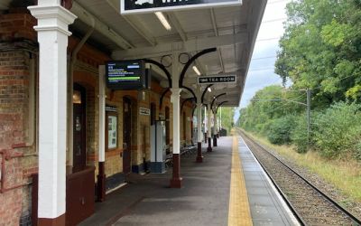 A colour photograph of the platform at Bricket Wood Station reveals brown and white paintwork and heritage benches and signs.
