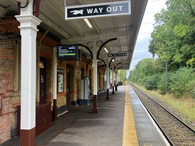 A colour photograph of the platform at Bricket Wood Station reveals brown and white paintwork and heritage benches and signs.