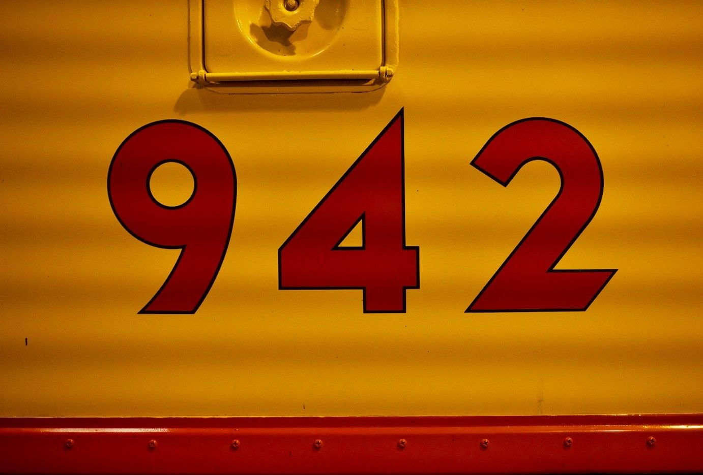 In this colour photograph, the number of a Union Pacific EMD E8 Diesel Locomotive ‘942’ appears in red sans-serif font against a yellow background.