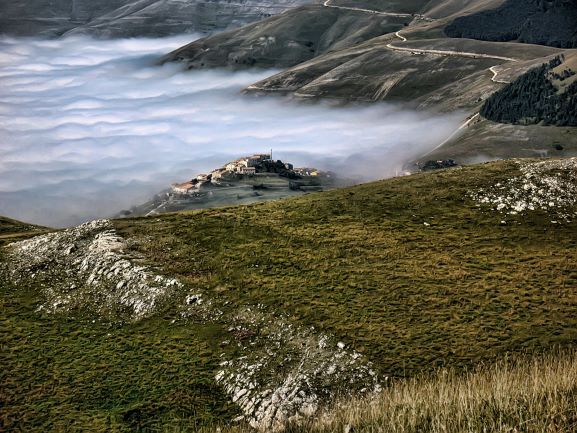 A photograph taken from a grassy mountaintop in the Marche reveals a mist-filled valley and the remote village of Castellúccio.