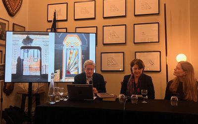 In this colour photograph Chris Schüler, Cath Harries and Melanie Backe-Hansen sit at a table with microphones and show illustrations from ‘Doors of London’ on a large screen.