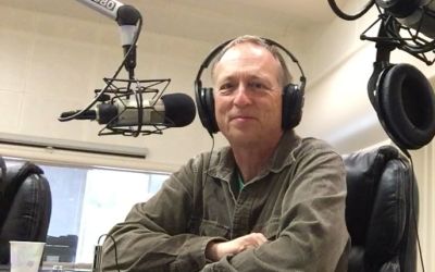 In this colour photograph Gary Shapiro, presenter of From the Bookshelf, wears headphones as he prepares to speak into a boom mike at his desk in KSCO radio station, Santa Cruz.