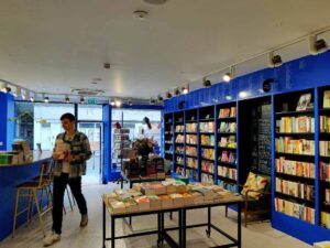 The manager carries a stack of books past the shop’s big blue counter.