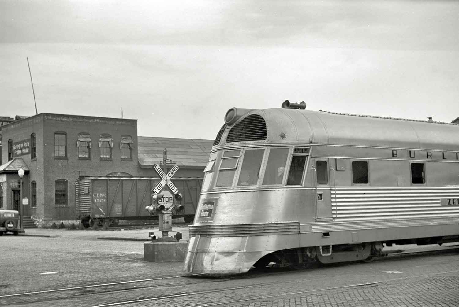 In this black-and-white photograph taken at La Crosse, Wisconsin, the Burlington’s streamlined Zephyr diesel express reaches a crossing, showing off its lightweight, stainless-steel construction.
