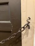In this close-up colour photograph taken in the hall of Dr Johnson’s house, a corkscrew latch on the door frame provides a secure fitting for the heavy chain stretched across the middle of the door. 