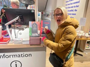 In this colour photograph a friend of Cath Harries points to a pile of ‘Doors of London’ she has just spotted by the checkout in Foyles bookshop, Charing Cross Road.