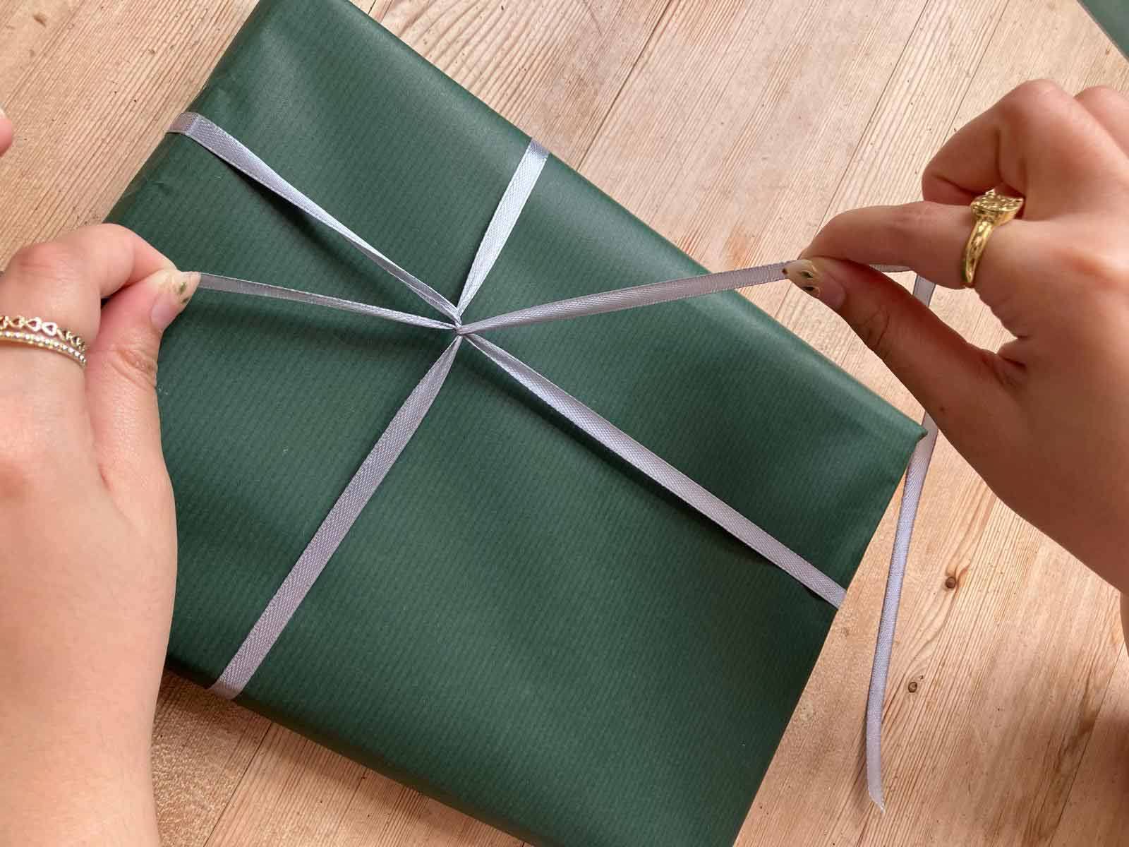 Colour photograph of a Sheldrake Press team member tying a silver ribbon round a parcel wrapped in sage green Kraft paper.