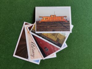 This colour image shows five railway-themed postcards on a green background arranged in a fan from top right to bottom left.
