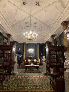 A colour photograph shot down the length of the Smoking Room at the National Liberal Club reveals a vast expanse of Turkey carpet, wood panelling, Corinthian columns, marble busts and oil portraits lit by brass chandeliers.