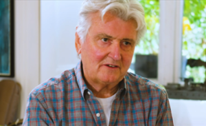 Wearing an open-neck checked blue shirt, the designer Ian Logan speaks during an interview about his book Logomotive.