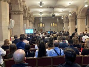 In this colour photograph taken from the back of the Livery Hall, a packed audience listens and watches slides on a flat screen as the City of London Corporation presents the case for redeveloping Liverpool Street Station. 