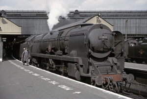 In this late-afternoon colour photograph taken by John Cosford in May 1964, a Merchant Navy Pacific locomotive heads a train at Waterloo Station, London.