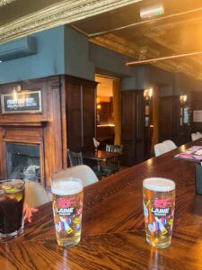 In this picture from the Ram Inn’s bar, a pair of pints are stood atop the wood-grain counter, with the wood panelled walls and fireplace visible in the background.