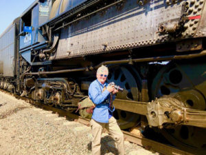 In this colour photograph Ian Logan stands with his camera beside Big Boy 4014, dwarfed by the driving wheels and gargantuan firebox. 