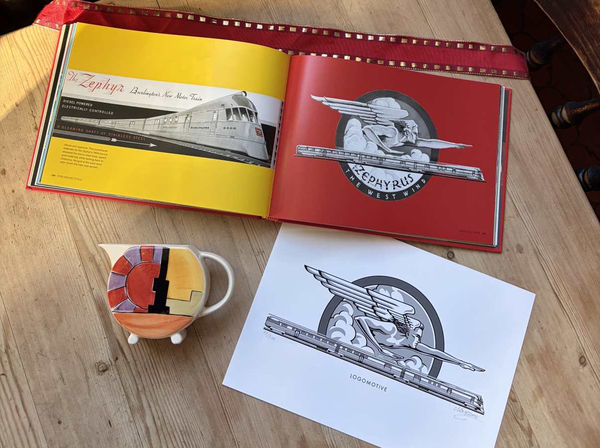 In this colour photograph, a copy of the book ‘Logomotive’ lies open at a page with a deep red background carrying the logo of the ‘Zephyr’ express train while alongside is a limited-edition black-and-white print of the same logo and an Art Deco milk jug.