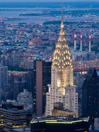 In this colour photograph the illuminated crown of the Chrysler Building rises above the Turtle Bay neighbourhood of Manhattan with the East River beyond.