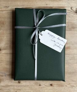 Colour photograph of white gift tag attached with silver twine to a book wrapped in sage green Kraft paper and tied with a silver ribbon.