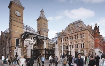 In this colour photograph commuters walk around the Bishopsgate entrance to Liverpool Street Station. The station was built in Victorian Gothic style with two brick towers on either side of the entrance.