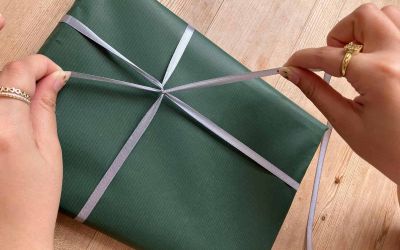 Colour photograph of a Sheldrake Press team member tying a silver ribbon round a parcel wrapped in sage green Kraft paper.