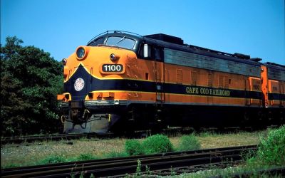 An F-Type Loco painted in orange, black and yellow livery hauls an excursion train on the Cape Cod Central Railroad.