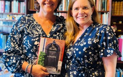 The door detectives Cath Harries and Melanie Backe-Hansen, dressed in similar blue-and-white patterned tops, hold a mock-up of their book Doors of London with an 18th-century door in Spitalfields on the cover.