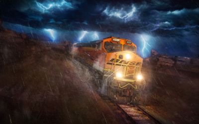 In this colour still from Train Sim World 3 a BNSF ES44C4 locomotive in its usual orange livery powers through the Cajon Pass in heavy rain. Lightning rages overhead.