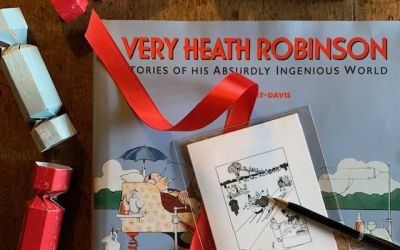 Colour photograph of a Very Heath Robinson book and a pack of six Winter Joys Christmas cards, surrounded by blue and red Christmas crackers.